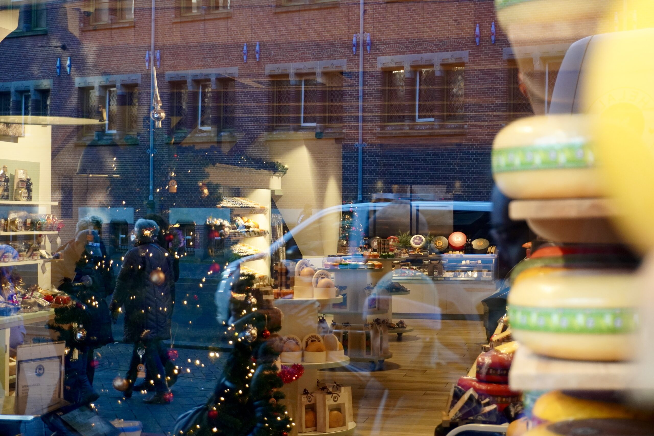 Christmas tree with lights in a window with reflections of people in a street